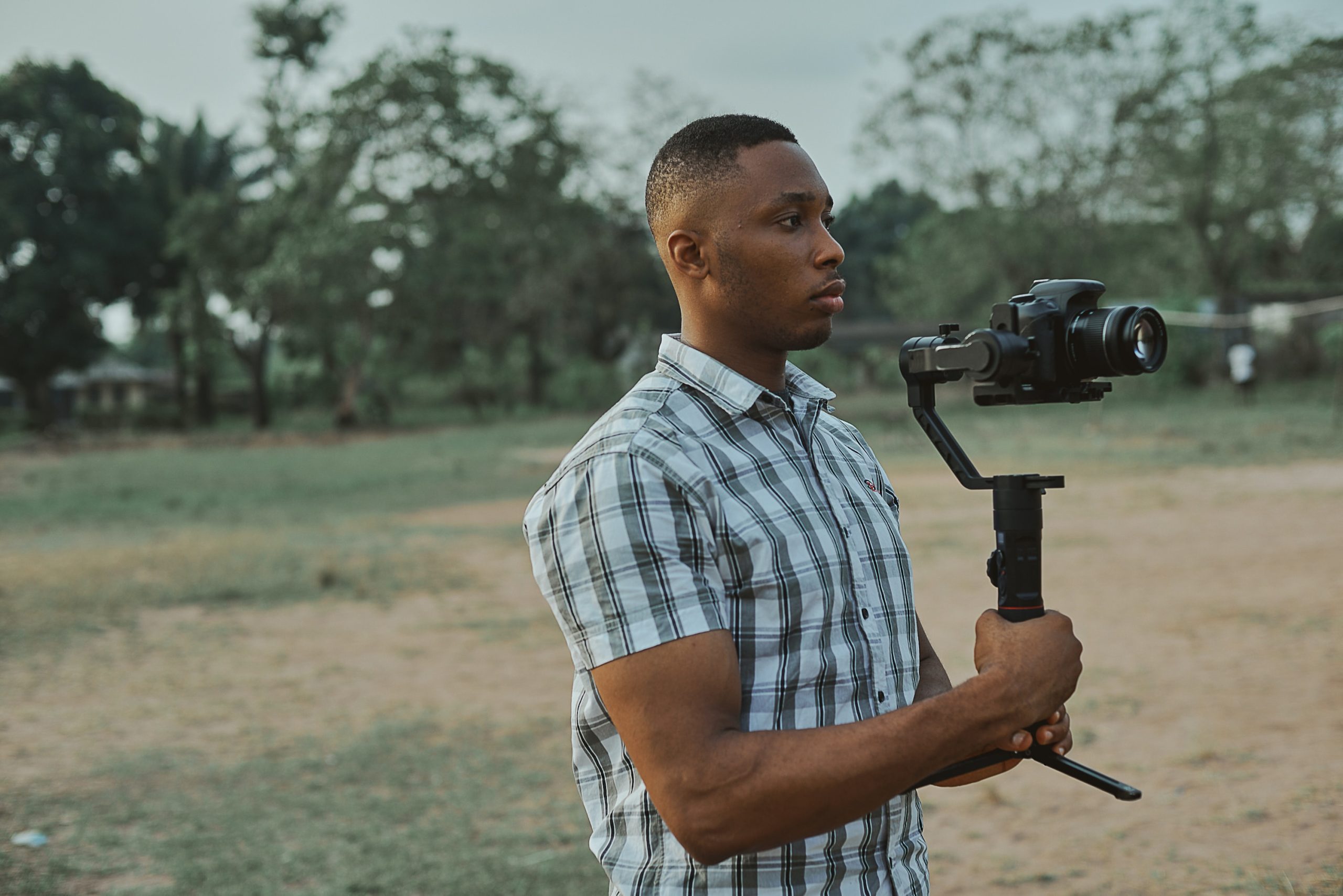 Filmmaker in Blue and White Plaid Button Up T-shirt Holding Black Dslr Camera on a gimbal. Get a Grip on your Video.