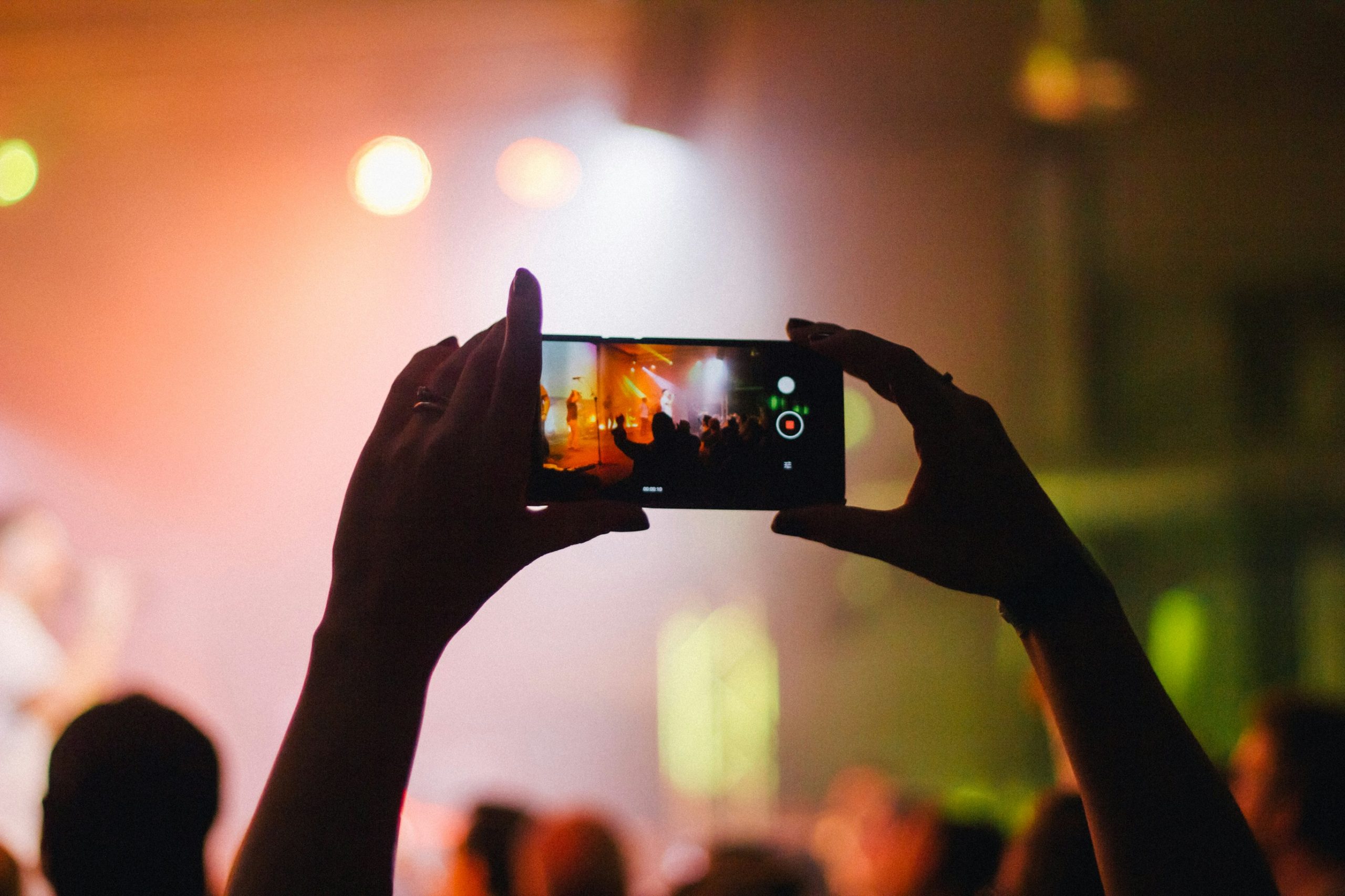 person holding smartphone while taking videos at live concert — you can do this if you learn live streaming